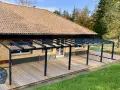 Drewniany taras zadaszony nowoczesną konstrukcją. Idealne rozwiązanie, czym zabudować boki tarasu, by stworzyć przytulną przestrzeń.