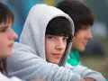 Drei Jungs, etwa 13 Jahre alt, sitzen nebeneinander. Einer trägt einen grauen Kapuzenpullover, der sein Gesicht fast verdeckt.