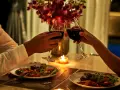 Para wznosząca toast kieliszkami z czerwonym winem podczas romantycznej kolacji przy świecach.