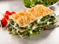 Deliciosa lasaña de verduras, con capas de pasta, espinacas y queso cremoso, acompañada de tomates cherry.