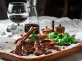 Saftige Lammkoteletts mit frischem Salat und einem Glas Rotwein. Die perfekte Wahl, welcher Wein zu Lamm passt, ist oft ein kräftiger Rotwein.