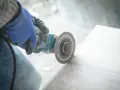 Ręka w niebieskiej rękawicy trzyma szlifierkę kątową, pokazując, jak ciąć płytki.