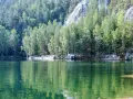 Zielona tafla jeziora odbija las i skalne miasto w Polsce. Ludzie spacerują po piaszczystym brzegu.