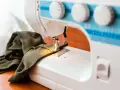 Maszyna do szycia z zieloną tkaniną. Zastanawiasz się, dlaczego maszyna do szycia zrywa górną nitkę? Może problem tkwi w igle lub naprężeniu?