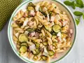 Un'insalata di pasta fredda sfiziosa con fusilli, zucchine grigliate, cubetti di prosciutto cotto e scaglie di formaggio.