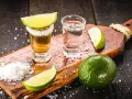 Zwei Gläser Tequila, Salz und Limettenspalten auf einem Holzbrett. Perfekt zum Tequila trinken.