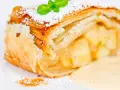 Ein Stück Apfelstrudel mit Filoteig, bestäubt mit Puderzucker und garniert mit Minze, serviert mit Vanillesauce.