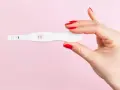 Dłoń z czerwonymi paznokciami trzyma test ciążowy z dwoma kreskami. To może być sygnał, że doszło do ciąży biochemicznej.