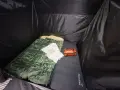 Schlafsack und Kissen auf der Isomatte, welche Seite oben ist, ist klar erkennbar. Ein kleines orangefarbenes Päckchen liegt daneben.