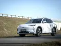 Biały SUV Geely E5 (EX5) na tle wiaduktu i niebieskiego nieba.