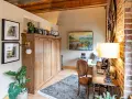 Accogliente angolo studio con un armadio a scomparsa in legno, un tappeto persiano e un quadro paesaggistico, che evoca l'atmosfera di una piccola casa di campagna.