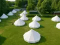 Malowniczy glamping nad morzem: białe namioty tipi na zielonej trawie, otoczone drzewami. Idealne miejsce na relaks.