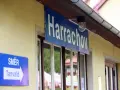 Tabliczka "Harrachov" nad oknami dworca. Obok znak kierunkowy "Směr Tanvald". Pociąg Szklarska Poręba Harrachov czeka na pasażerów.