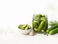 Słoik pełen ogórków kiszonych i miseczka pokrojonych, obok świeże ogórki, czosnek i koperek. Czy ogórki kiszone są zdrowe? Tak, to naturalny probiotyk!