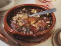 Un plat en terre cuite débordant de haricots blancs, de morceaux de viande dorée et de saucisses, prêt à être dégusté. La recette du vrai cassoulet traditionnel, un délice réconfortant.