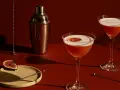 Elegancki drink z czerwonym winem, ozdobiony plasterkiem cytrusa, obok shakera i kieliszka z pianką.