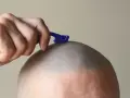 Mano con maquinilla azul afeitándose la cabeza, dejando la piel suave y sin vello.