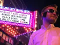 Mann im Elvis-Stil mit Sonnenbrille vor der "Blues City Band Box"-Neonreklame, die "Black Elvis" ankündigt.