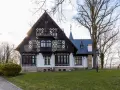 Pałac myśliwski w Promnicach, z charakterystyczną architekturą szachulcową i zdobieniami, otoczony drzewami.