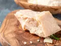 Kawałek twardego sera Grana Padano na desce z oliwnego drewna. Czy Grana Padano to parmezan? To pytanie często zadawane przez miłośników włoskich serów.