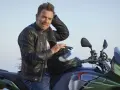 Ewan McGregor, con giacca di pelle, posa su una Moto Guzzi verde e grigia, pronto per un'avventura.