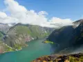 Malownicze rejsy po fiordach norweskich z Polski. Zielone zbocza gór schodzą do turkusowej wody, chmury otulają szczyty.
