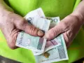 Dłonie trzymają polskie banknoty. Nowe zasady przyznawania renty socjalnej mogą wpłynąć na finanse wielu osób.