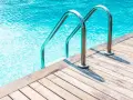 Escalera de piscina de obra con barandillas cromadas sobre tarima de madera. ¿Cuánto cuesta una piscina de obra?