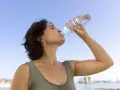Donna beve acqua per combattere il caldo e la depressione, con il cielo azzurro sullo sfondo.