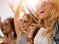 Trois amies profitent d'un festival ensoleillé, leurs rires atteignant un niveau sonore équivalent à 66 décibels.