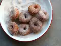 Små, nybakade donuts som rullats i socker och kanel ligger i en vit skål med röd kant.