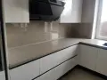 Nowoczesna kuchnia z frontami w kolorze ral9001 i eleganckim, jasnym blatem. Czarny okap dodaje charakteru.