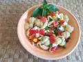 Un'appetitosa insalata di pasta vegetariana con pomodorini, piselli, mais e mozzarella, guarnita con basilico fresco.