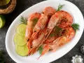 Plato blanco con langostinos cocidos, rodajas de limón y eneldo. Ideal para recetas con langostinos.
