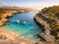 Malownicza zatoka na największej wyspie balearów. Turkusowa woda, piaszczysta plaża, łodzie i kręta droga wzdłuż klifu.