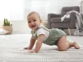 Uśmiechnięte 8-miesięczne dziecko raczkuje po dywanie. Zwróć uwagę na jego rozwój, gdy powinno niepokoić.