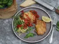 Piccata Milanese: goldbraunes Schnitzel mit Spaghetti in Tomatensauce, garniert mit Rucola und Zitrone.