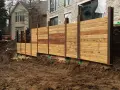 Solidny murek oporowy z drewna, budowany przy użyciu koparki, zabezpiecza skarpę przy nowoczesnym domu.