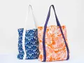Deux sacs fourre-tout aux motifs vibrants : un bleu avec des éventails blancs, l'autre orange avec des feuilles de palmier blanches. Un patron de sac gratuit à télécharger pour créer vos propres accessoires.