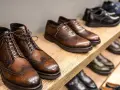 Scarpe marchigiane famose: eleganti stivaletti e stringate in cuoio marrone, con dettagli traforati, su uno scaffale di legno.