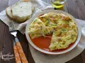 Una soffice frittata di albumi con erbe aromatiche, servita su un piatto arancione, accanto a fette di pane tostato e una forchetta.
