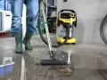 Person i gröna stövlar använder en Kärcher WD 6 för att suga upp vatten från ett betonggolv i ett garage.