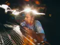 Un disc jockey célèbre, concentré, manipule une console de mixage dans un studio d'enregistrement, baigné de lumières vives.