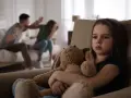 Ein trauriges Mädchen hält seinen Teddybär, während im Hintergrund Eltern streiten. Eine blitzscheidung ohne trennungsjahr hinterlässt Spuren.