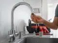 Dłoń trzymająca wyczyszczony aerator kranu, z którego kapie woda.