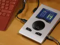 Srebrny interfejs audio RME Babyface Pro FS podłączony do czerwonej klawiatury. Idealny do mobilnego studia.