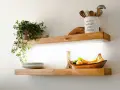Estantes de madera con iluminación LED oculta, ideal para saber como colocar tiras led en estantes. Exhiben plantas, vajilla y frutas.