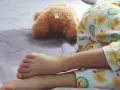 Ein Kind schläft im Pyjama mit Entenmuster, ein Teddybär liegt daneben. Es ist ein friedlicher Moment, in dem das Kind nachts ein und merkt es nicht.