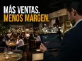 Hombre revisa tablet con gráficos de ventas y margen operativo en un restaurante lleno, buscando mejorar la rentabilidad del restaurante.