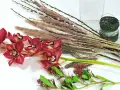 Ciemnoróżowe orchidee, trawy, pióra i gałązki tworzą kompozycję zrównoważoną.